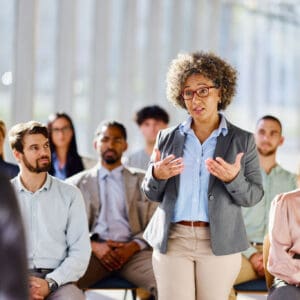Woman speaking to seated audience in meeting.
